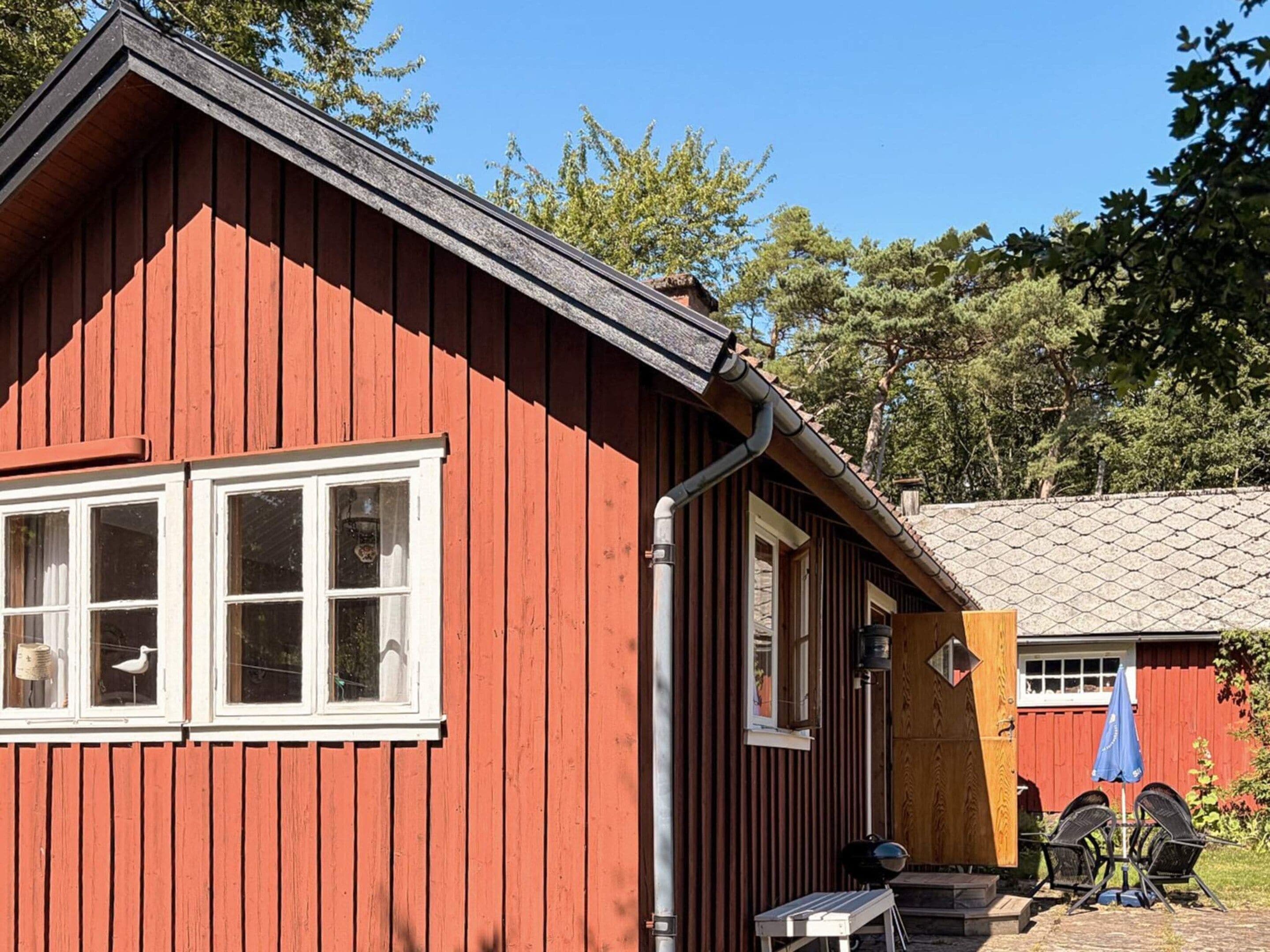 A red wooden building with white-framed windows, a door, and a small outdoor seating area with a table and chairs.