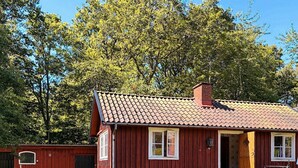 Una casa de madera roja con techo de tejas, un banco y una parrilla en el exterior.