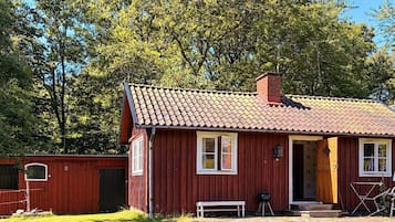 A red wooden house with a tiled roof, a bench, and a grill outside.