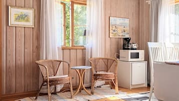 A cozy room with wooden walls, a window with curtains, two wicker chairs, a small table, a microwave, and a painting on the wall.