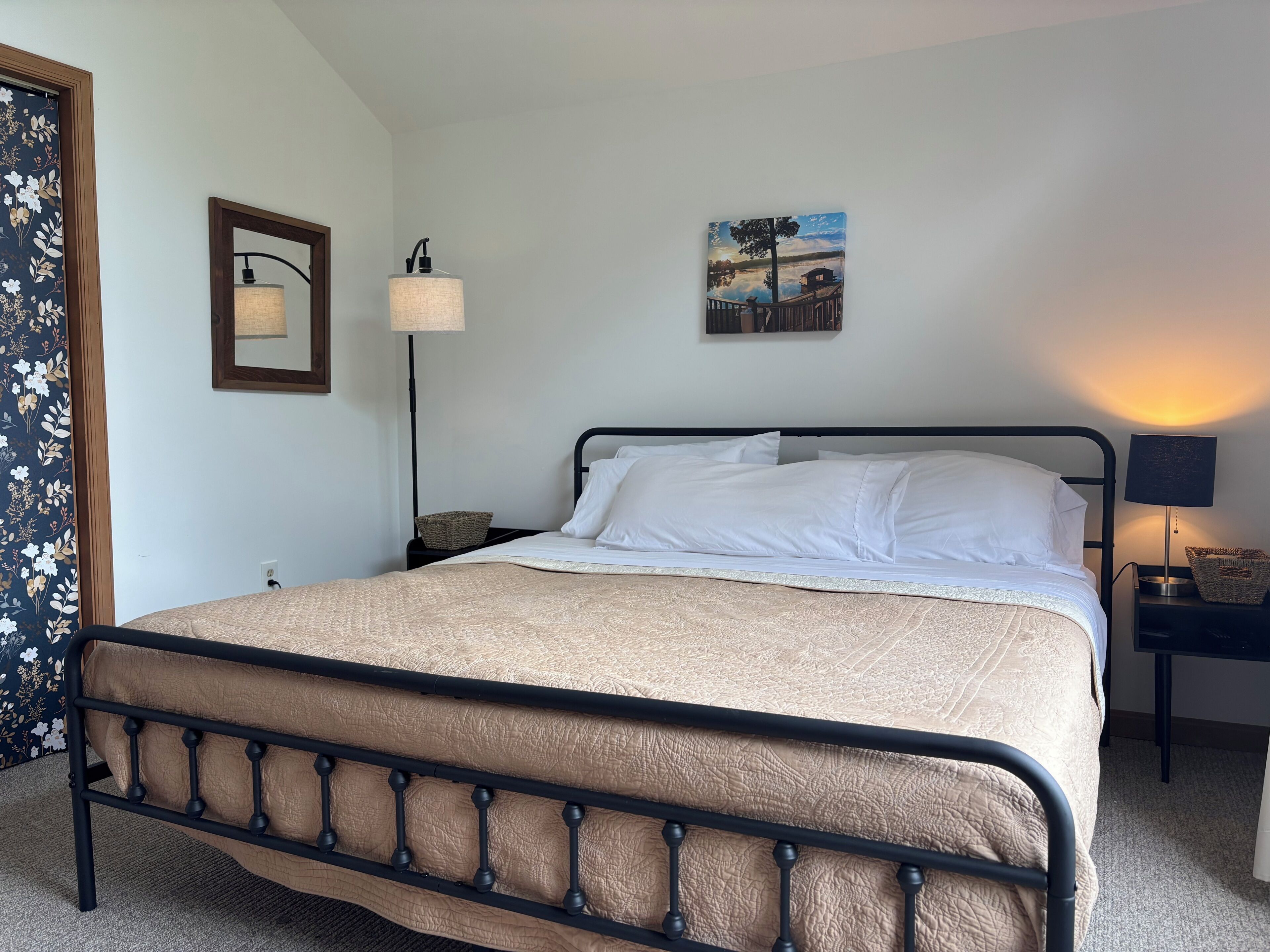 Un lit bien fait, avec une tête de lit, une lampe de chevet, un tableau accroché au mur et une lampe sur pied.