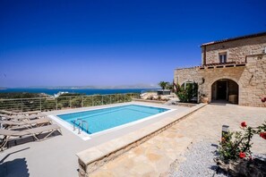 Ein Pool mit Meerblick, ein Steinhaus und ein Blumengarten.