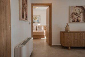 A hallway leading to a bedroom with a bed, a radiator, and a wooden cabinet with a vase. - Luxury Villa with unlimited sea view (Chania)