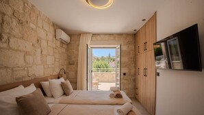 Quarto de hotel com parede de pedra, cama com cabeceira, televisão fixada na parede e varanda com vista.