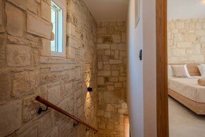 A stone-walled staircase leading to a bedroom with a bed and a window. - Luxury Villa with unlimited sea view (Chania)