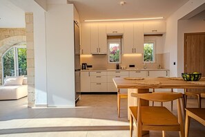 Eine moderne Küche mit weißen Schränken, einem Holztisch und Blick ins Freie.