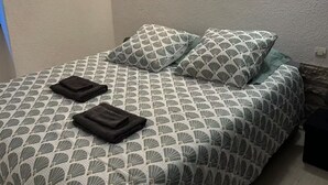 Ein Bett mit einem gemusterten Überwurf, zwei Kissen und zwei gefaltete Handtücher.
