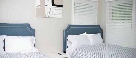 Habitación de hotel con dos camas, una mesita de noche y un cuadro abstracto colgado en la pared.