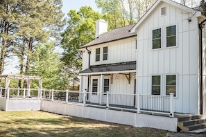 A two-story white house with a porch, a covered patio, and a fenced yard.
