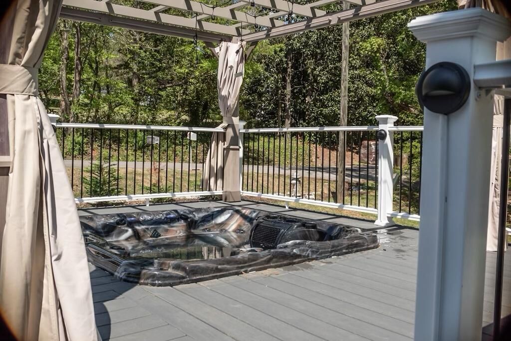 Zona de hidromasaje al aire libre con techo, una pérgola, barandilla blanca y vistas a la carretera y árboles.