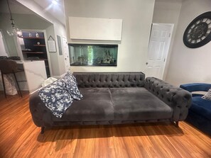 A living room with a tufted sofa, a wall-mounted aquarium, and a dartboard.