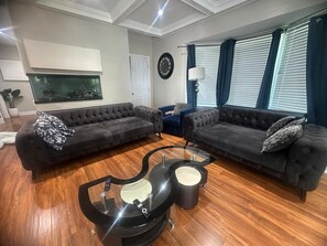Ein Wohnzimmer mit zwei dunklen Sofas, einem Glastisch und einer Wanduhr.