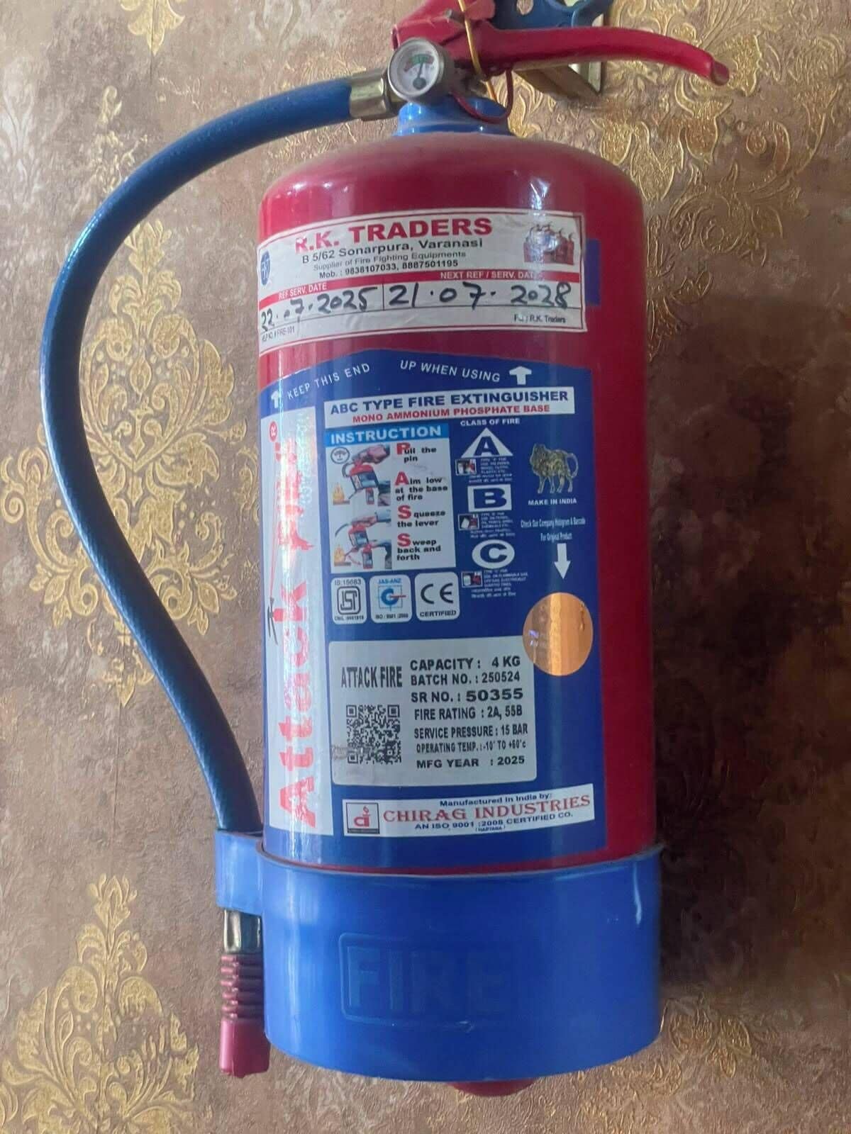 A fire extinguisher with a red and blue body, mounted on a wall with a decorative pattern.