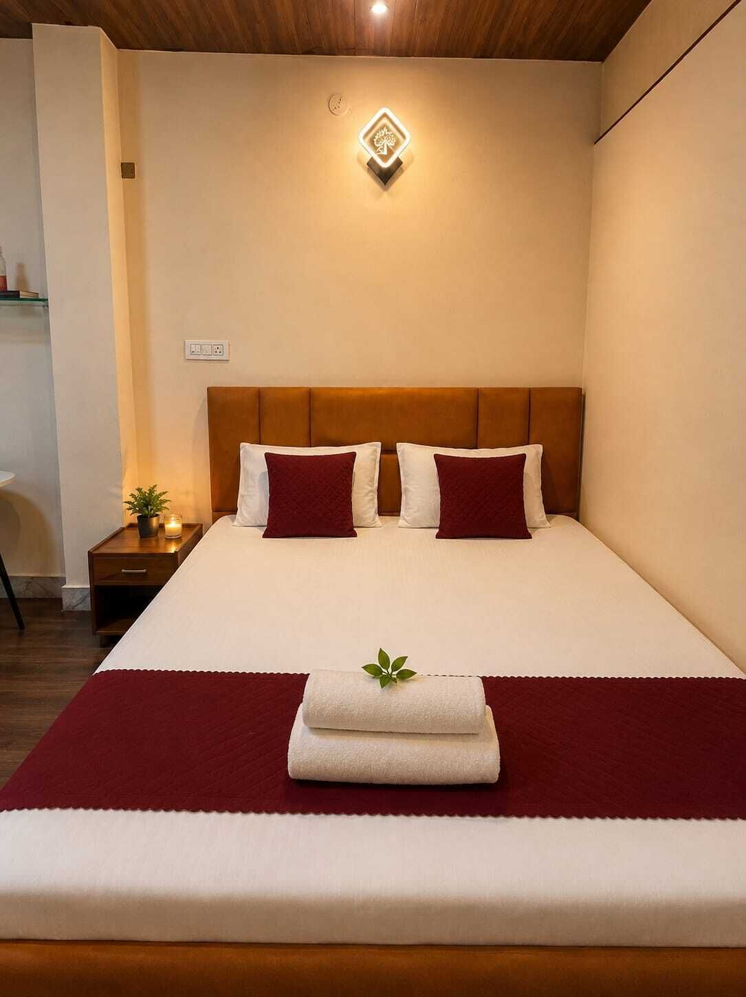 A neatly made bed with a headboard, a bedside table with a plant, and a wall-mounted light fixture.