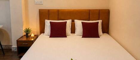 A neatly made bed with a headboard, a bedside table with a plant, and a wall-mounted light fixture.