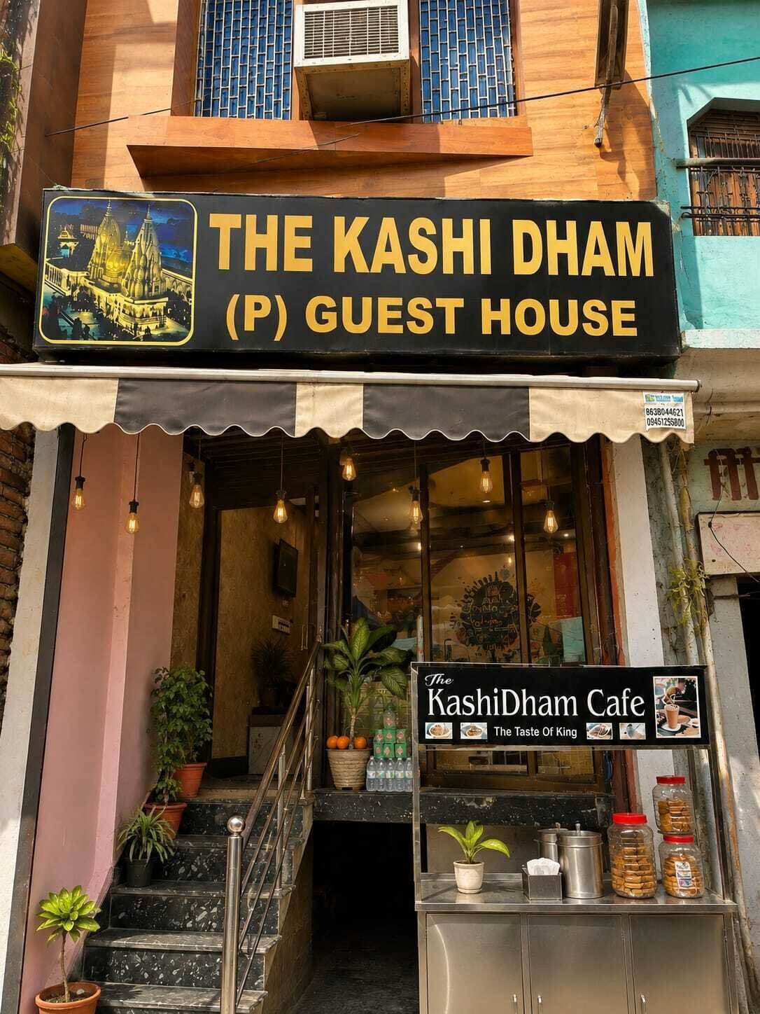 A guest house named 'The Kashi Dham (P) Guest House' with a signboard featuring a temple illustration.