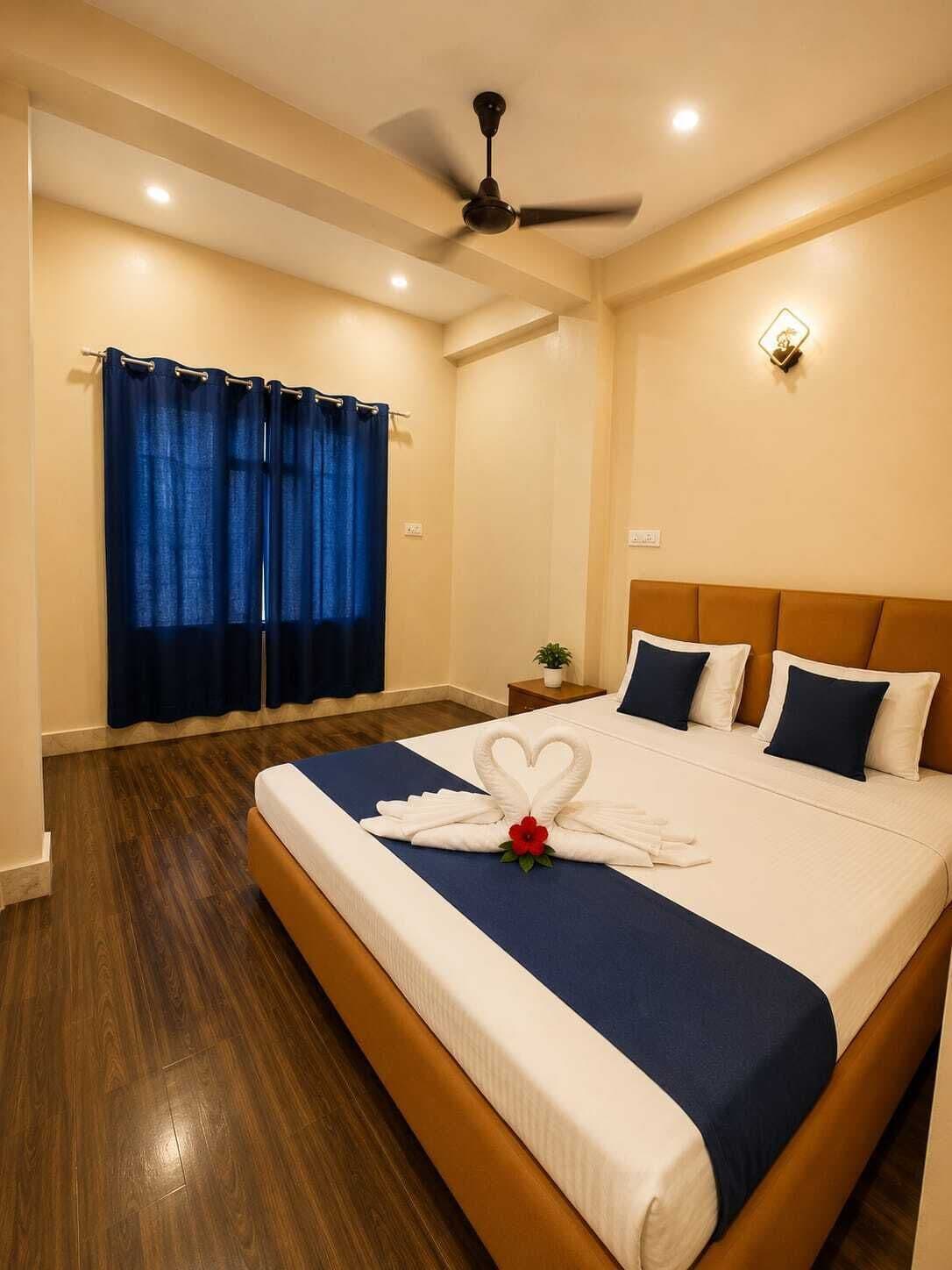 Habitación de hotel con una cama grande, un ventilador de techo, una mesita de noche con una planta y una ventana con cortinas azules.