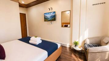Habitación de hotel con cama, una silla, una mesita con una planta, un cuadro en la pared y un espejo.
