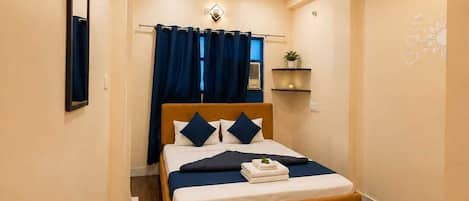 Ein Schlafzimmer mit einem Bett, einem Spiegel, einem Deckenventilator und einem kleinen Regal mit einer Pflanze.