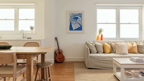 A living room with a wooden dining table, a sofa, and a guitar. - Large Two-Bedroom Garden Apartment (North Bondi)