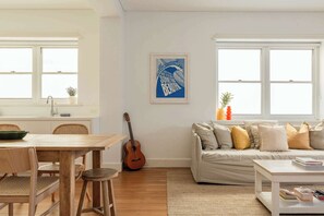A living room with a wooden dining table, a sofa, and a guitar. - Large Two-Bedroom Garden Apartment (North Bondi)