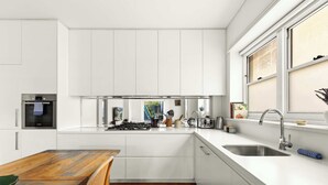 A modern kitchen with white cabinetry, a built-in oven, and a large window. - Large Two-Bedroom Garden Apartment (North Bondi)