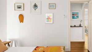 A bedroom with a bed, a wooden headboard, a wall-mounted shelf, and a door leading to another room. - Large Two-Bedroom Garden Apartment (North Bondi)