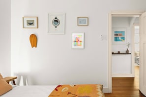 A bedroom with a bed, a wooden headboard, a wall-mounted shelf, and a door leading to another room. - Large Two-Bedroom Garden Apartment (North Bondi)