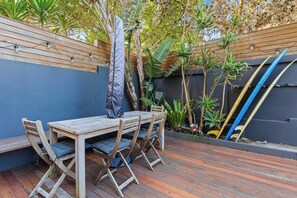 An outdoor patio with a wooden table and chairs, surrounded by plants and a wooden fence. - Private Garden Apartment near Bondi Beach (North Bondi)