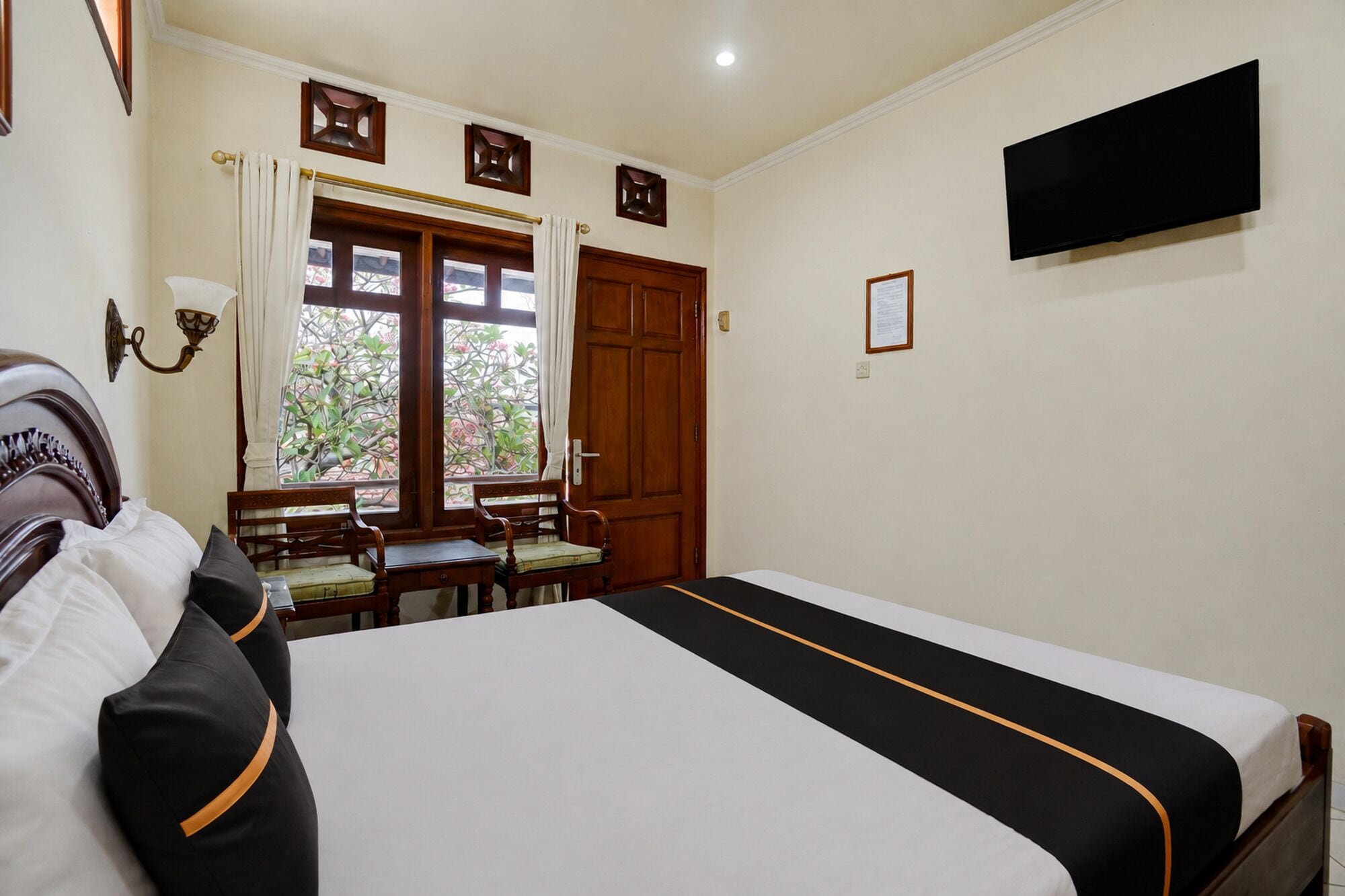 A hotel room with a bed, a desk, two chairs, a television, and a window with curtains.