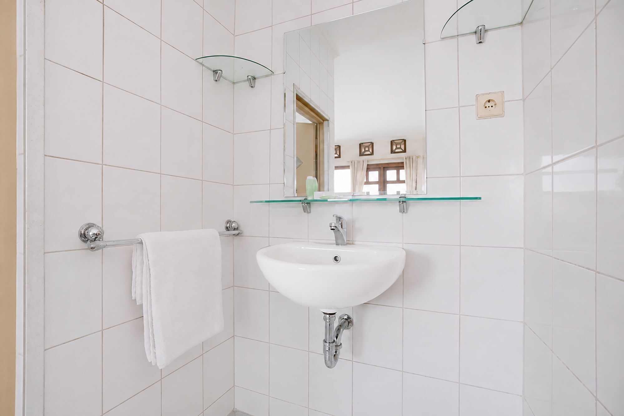 Une salle de bain avec un lavabo blanc, une étagère en verre au-dessus et une serviette suspendue à un porte-serviettes.