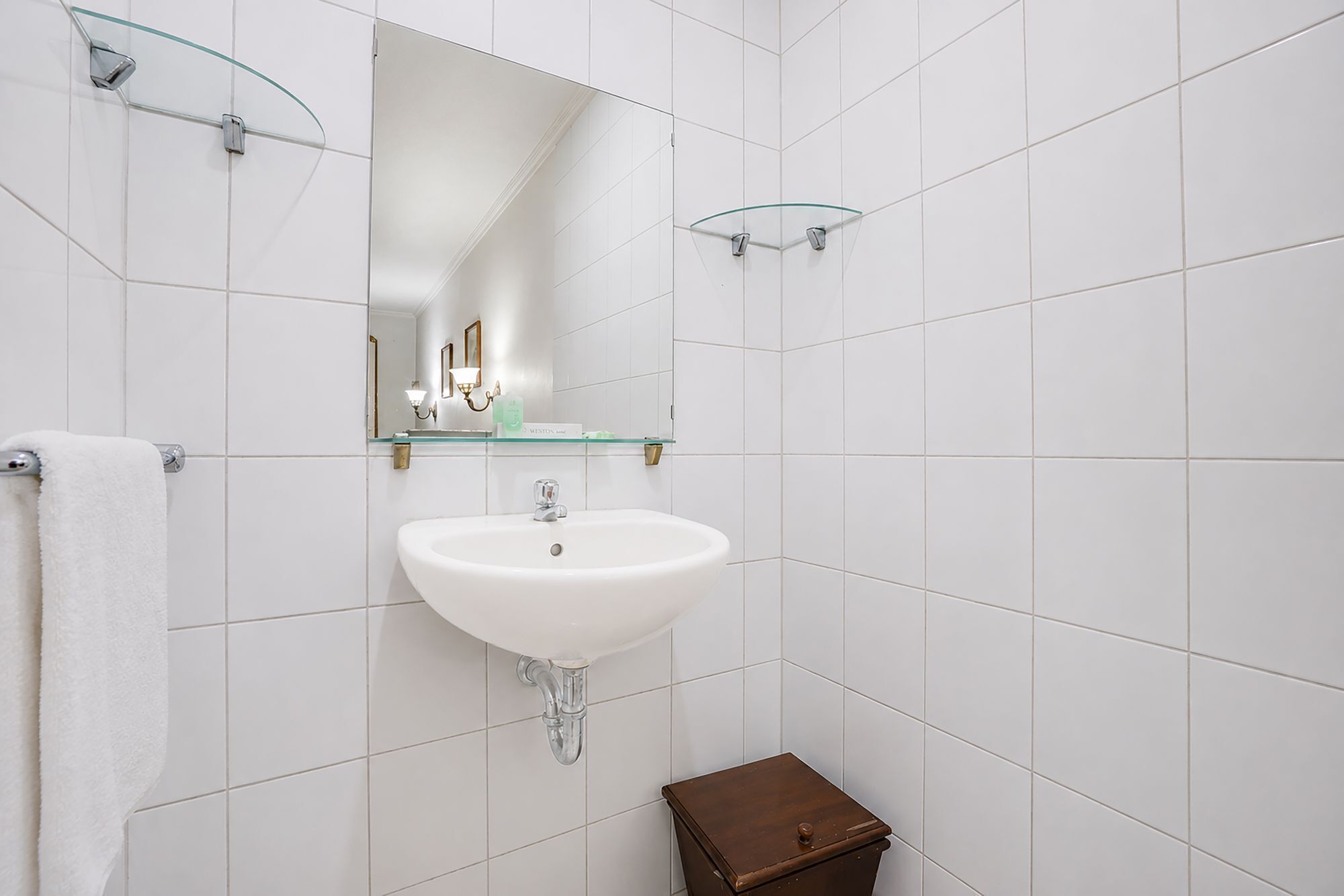 Une salle de bain avec un lavabo blanc, une cabine de douche en verre et un petit meuble en bois.