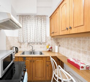 A compact kitchen with wooden cabinets, a stainless steel sink, a microwave, and a stove. - Athens Metro Escape - Central & Connected by ΜΡS (Athina)