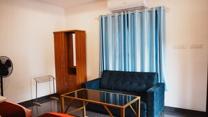 A room with a blue sofa, a wooden wardrobe, a glass table, and a ceiling fan.