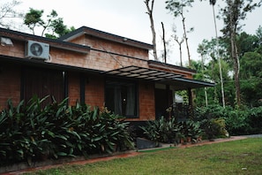A modern house with a brick exterior, a covered porch, and lush greenery surrounding it. - Coffeepolo Resorts Wayanad (Thirunelly)