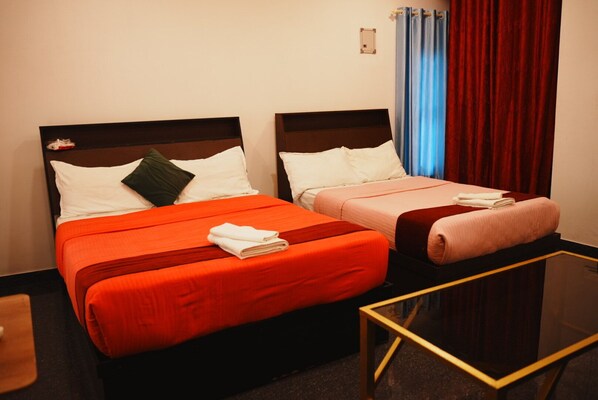 Dos camas con ropa de cama roja y rosa, una mesita y una cortina.