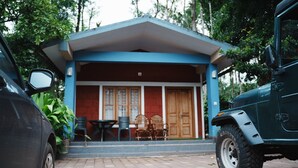 A building with a covered porch, a table and chairs, and a parked vehicle.