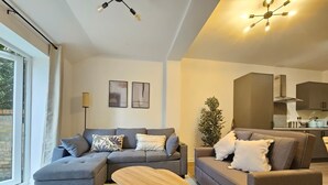 A modern living room with a sectional sofa, a coffee table, and a potted plant. - Luxury Flat 10 Mins from Station + Bike ! (Cambridge)