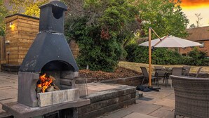 Un patio esterno con un forno per pizza in pietra, un tavolo con sedie e un ombrellone grande.