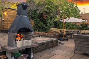 Un patio al aire libre con un horno de pizza de piedra, una mesa con sillas y un gran paraguas.