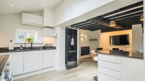 A modern kitchen with white cabinetry, a black refrigerator, and a dining area with a TV. - Stargazing copper tub backing onto RSPB reserve (Cambridge)