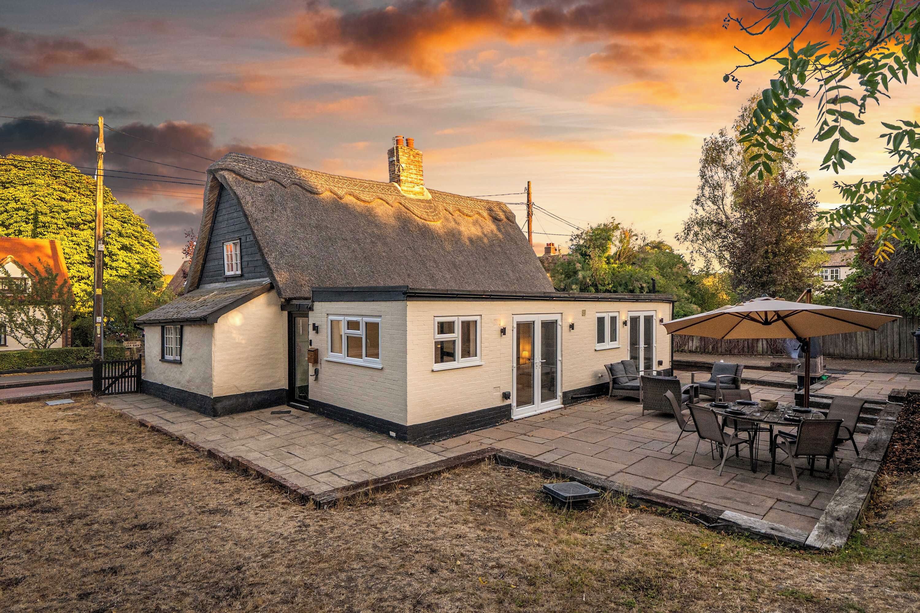 Een huis met rieten dak, een patio met tuinmeubilair en uitzicht op de lucht.
