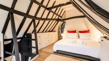A bedroom with a sloped ceiling, a bed with white bedding and red pillows, a wooden ladder, and a white dresser.