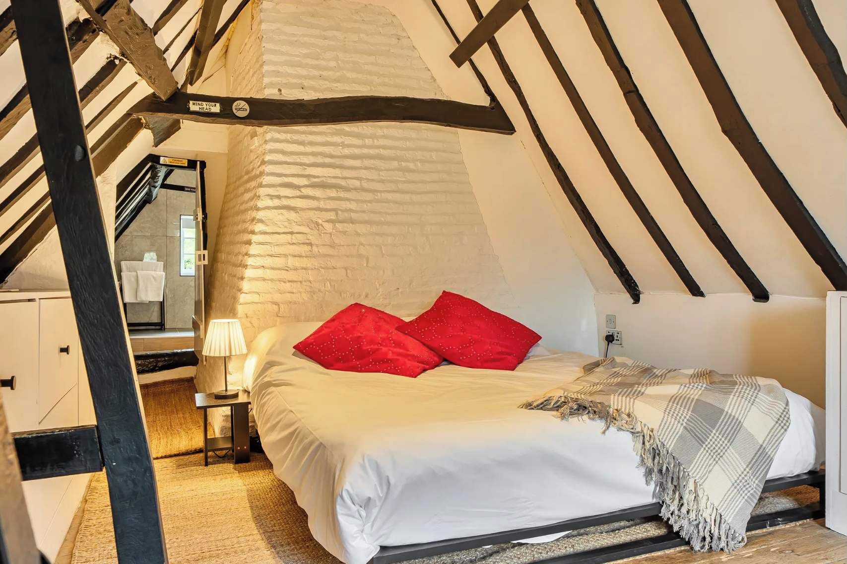 Attic Bedroom: Characterful space with exposed beams, cream walls, a double bed topped with bold red pillows, warm wood 