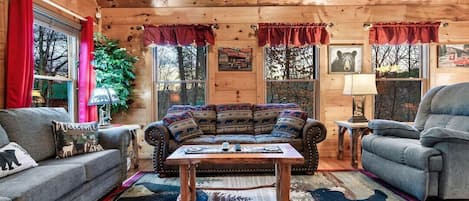 Interior acogedor de una cabaña con techo de madera, un sofá, una silla y una mesita de centro.