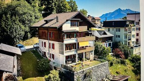 Un immeuble à plusieurs étages doté de balcons, d’un mur en pierre et avec une montagne en arrière-plan.