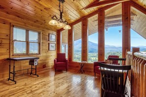 Ein Holzhütten-Interieur mit Schreibtisch, Stühlen und großen Fenstern mit Blick auf die Berge.