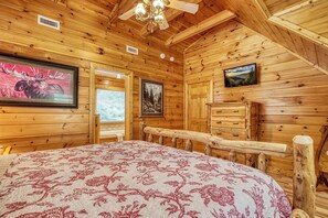 Ein Holzblockhaus-Interieur mit einem Bett, einer Kommode und einem Fernseher an der Wand.