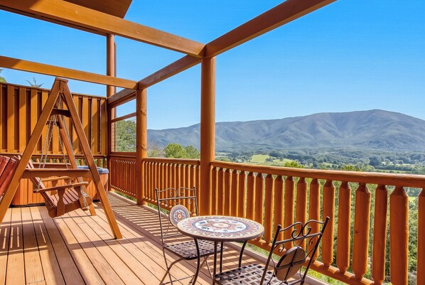 Eine Holzterrasse mit Tisch und Stühlen mit Blick auf eine gebirgige Landschaft.