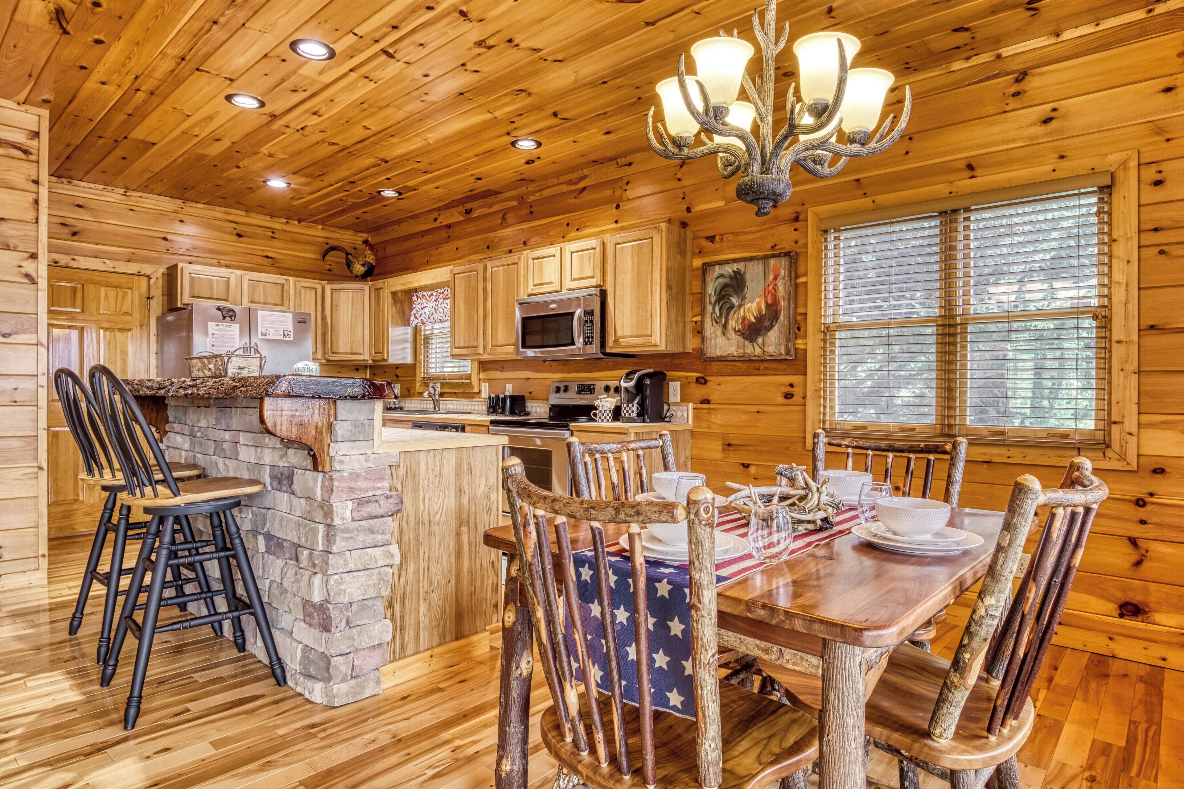 L’intérieur d’un chalet en bois rustique comprend une cuisine, un coin repas et un lustre.